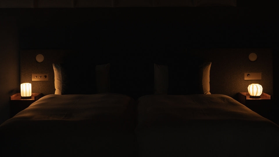 Japanese Paper Table Lamp "Flower of Light M" lit on a wooden bedside table