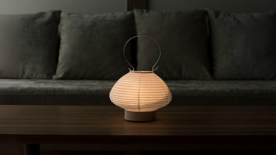 Japanese paper table lamp shaped like a lantern emitting a warm glow on a wooden table in a living room