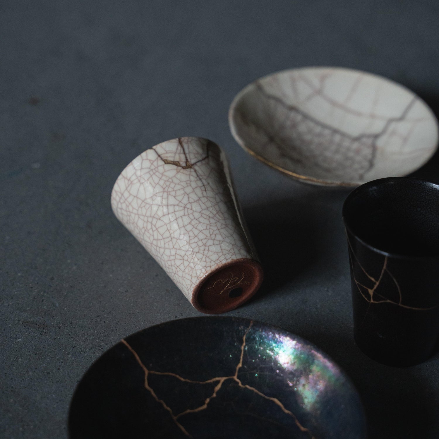 White and black kintsugi cups and bowl, showcasing the traditional Japanese art of repairing broken pottery with gold lacquer.