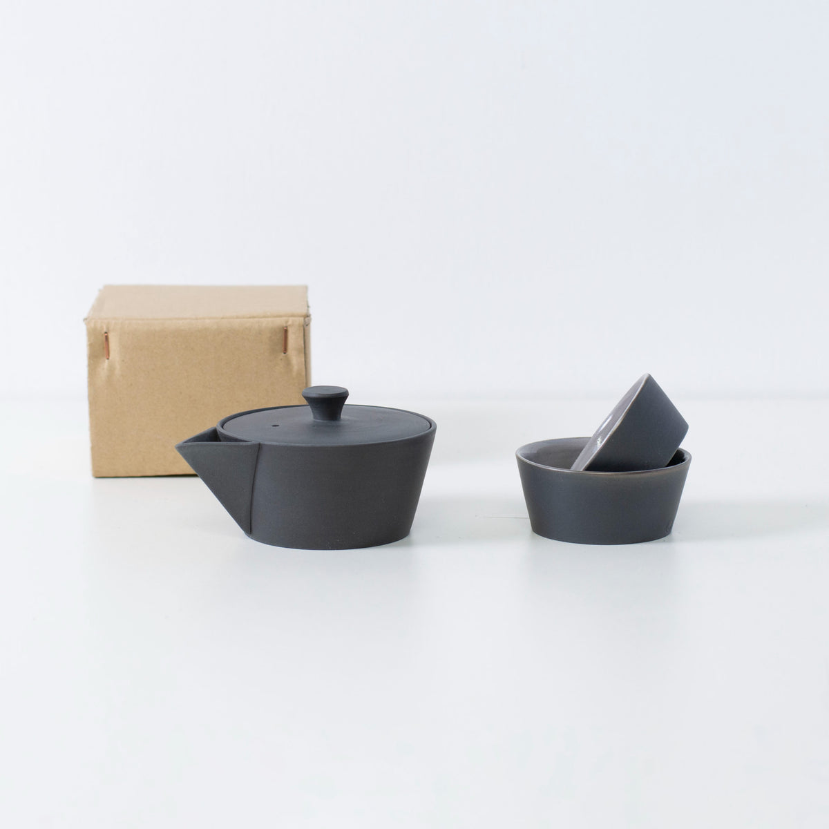 "Ensemble de thé empilable Banko-yaki japonais avec une théière noire et deux tasses, présenté dans une simple boîte en papier."