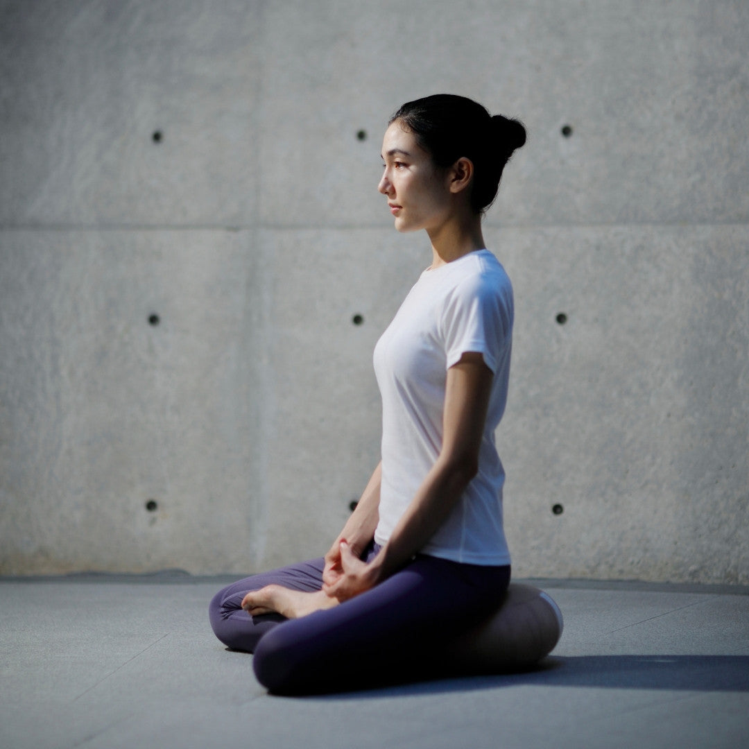 A woman sitting in the lotus position and meditating with a Japanese Meditation Cushion Zafu