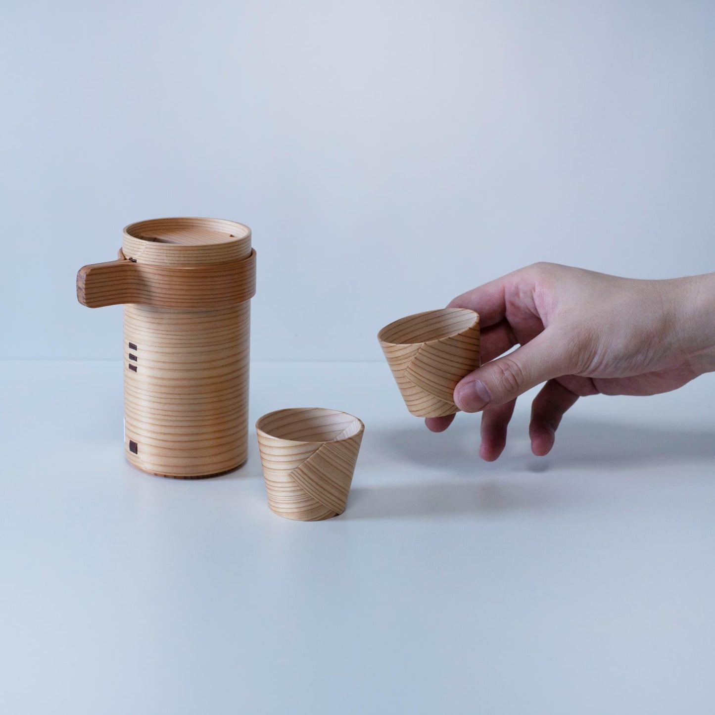Hand holding a gift set of Akita cedar sake pitcher and cups, crafted by a 76-year-old craftsman using traditional Magewappa bending techniques.