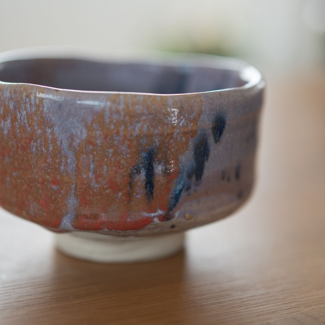 Close-up image showcasing the dramatic Navy and Red Splash glaze on the handmade matcha chawan, emphasizing the texture and pale purple Kinyo glaze base by Shinzan Kiln.