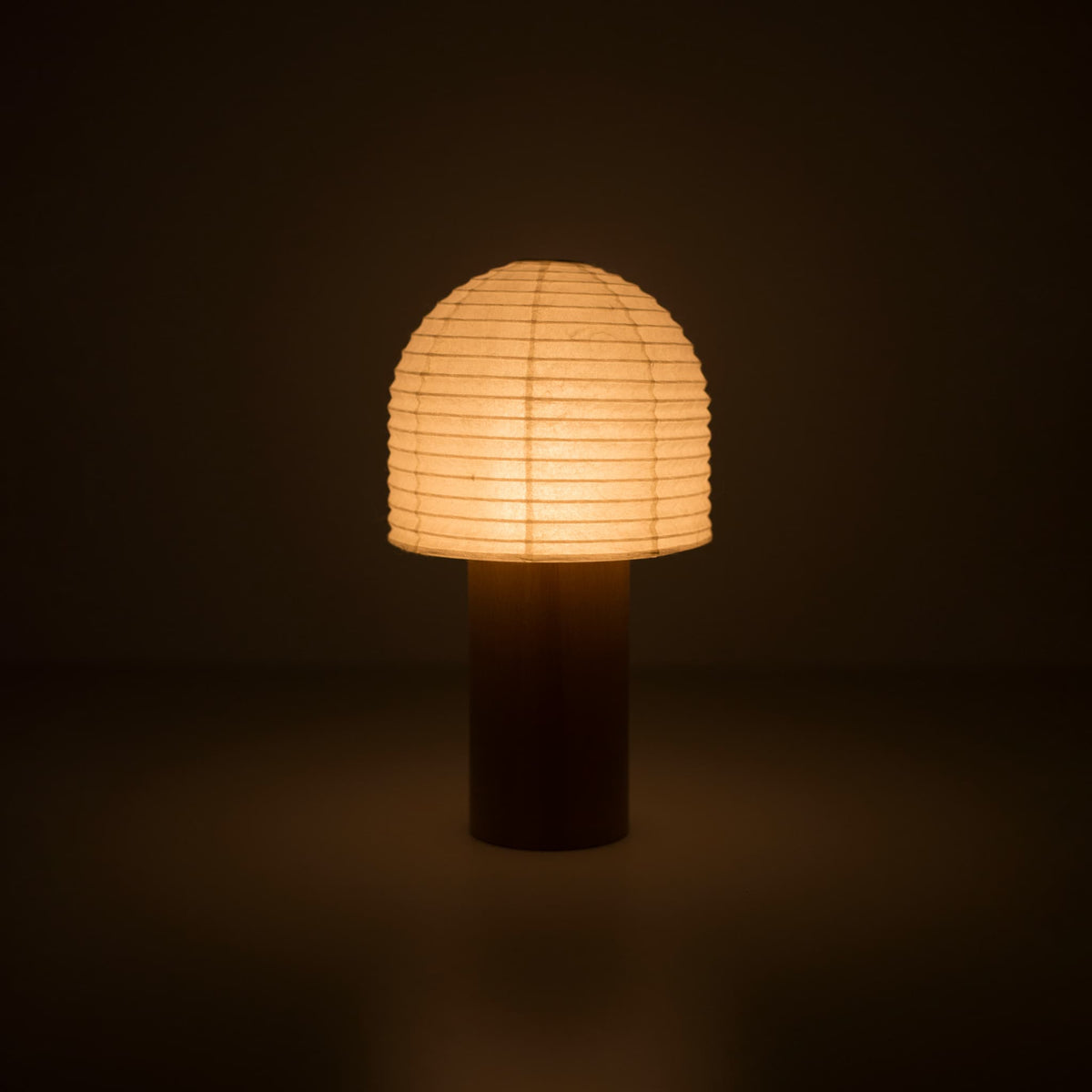 A portable Japanese paper lantern with a wooden handle and bell-shaped top, glowing warmly in a dark room