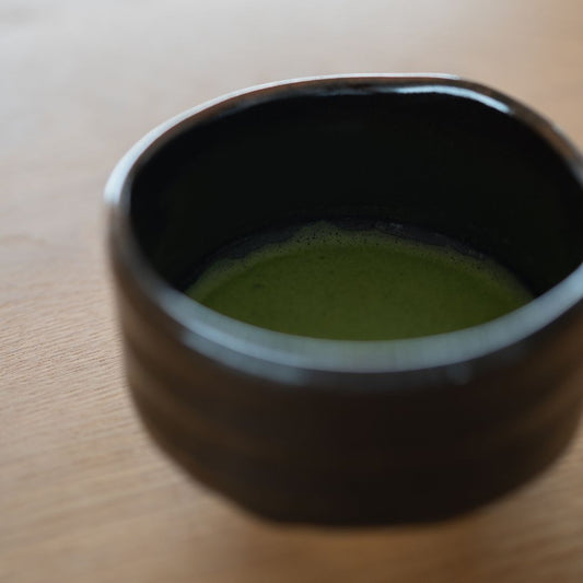 Close-up of vibrant emerald green matcha tea foam inside the deep black Japanese chawan bowl.