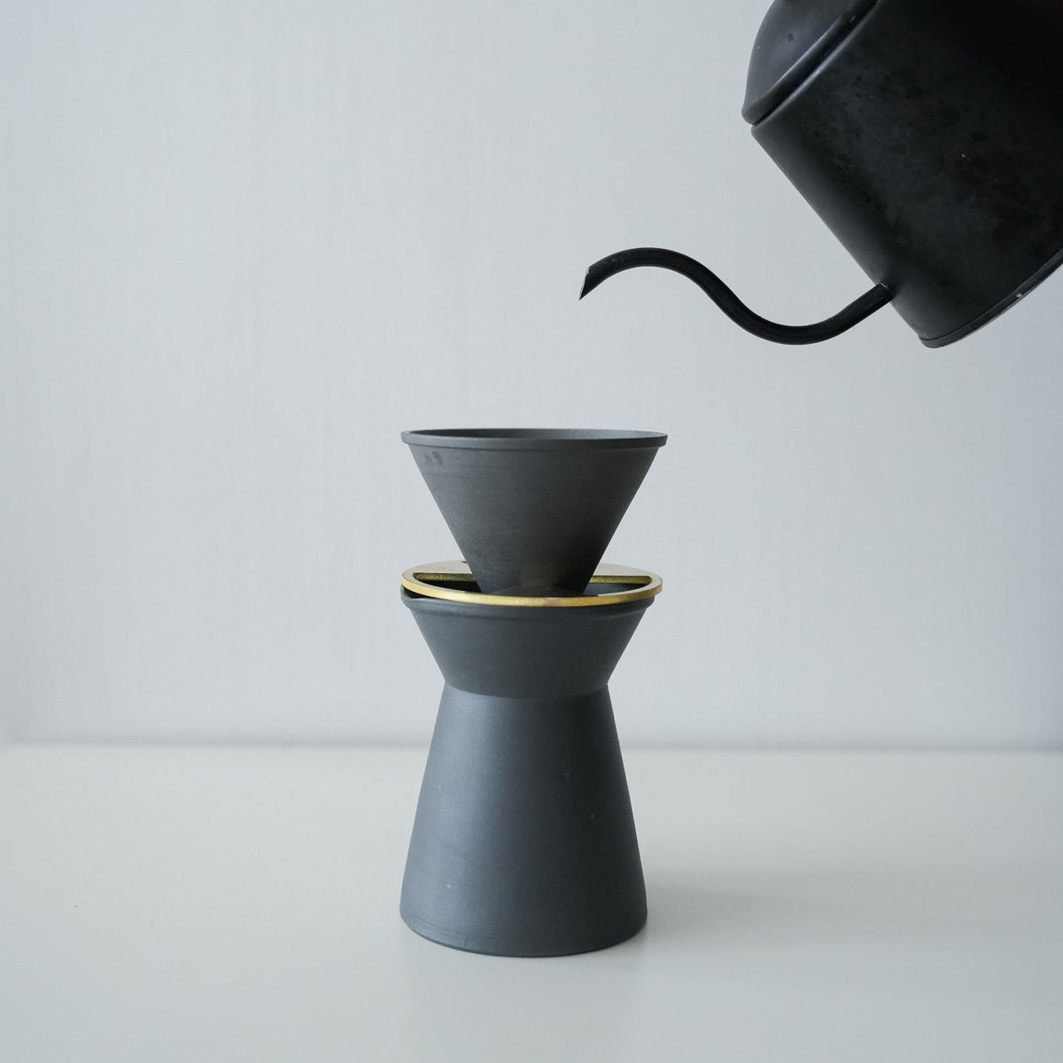 Verser de l'eau chaude d'une bouilloire noire dans un ensemble minimaliste de cafetière et de filtre Banko ware noirs.