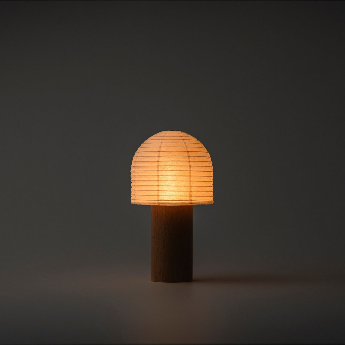 A brightly glowing Japanese paper lantern with a bell-shaped paper top and wooden handle in a dark room