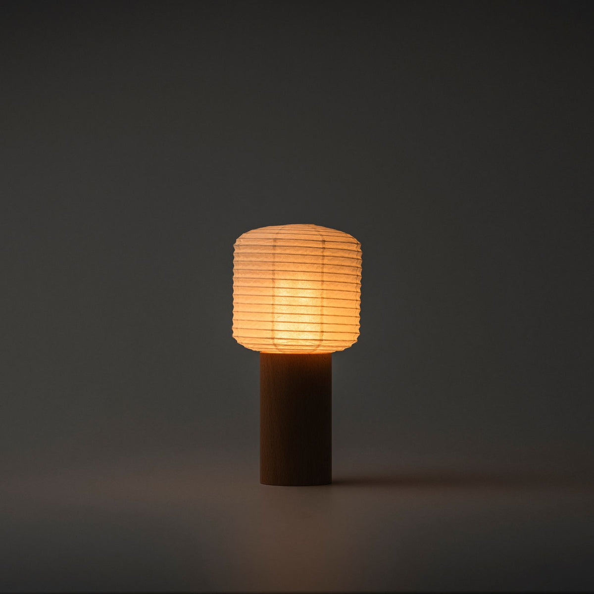 Een draagbare papieren tafellamp die fel warm licht uitstraalt in een donkere kamer, met een houten handvat en papieren bovenkant