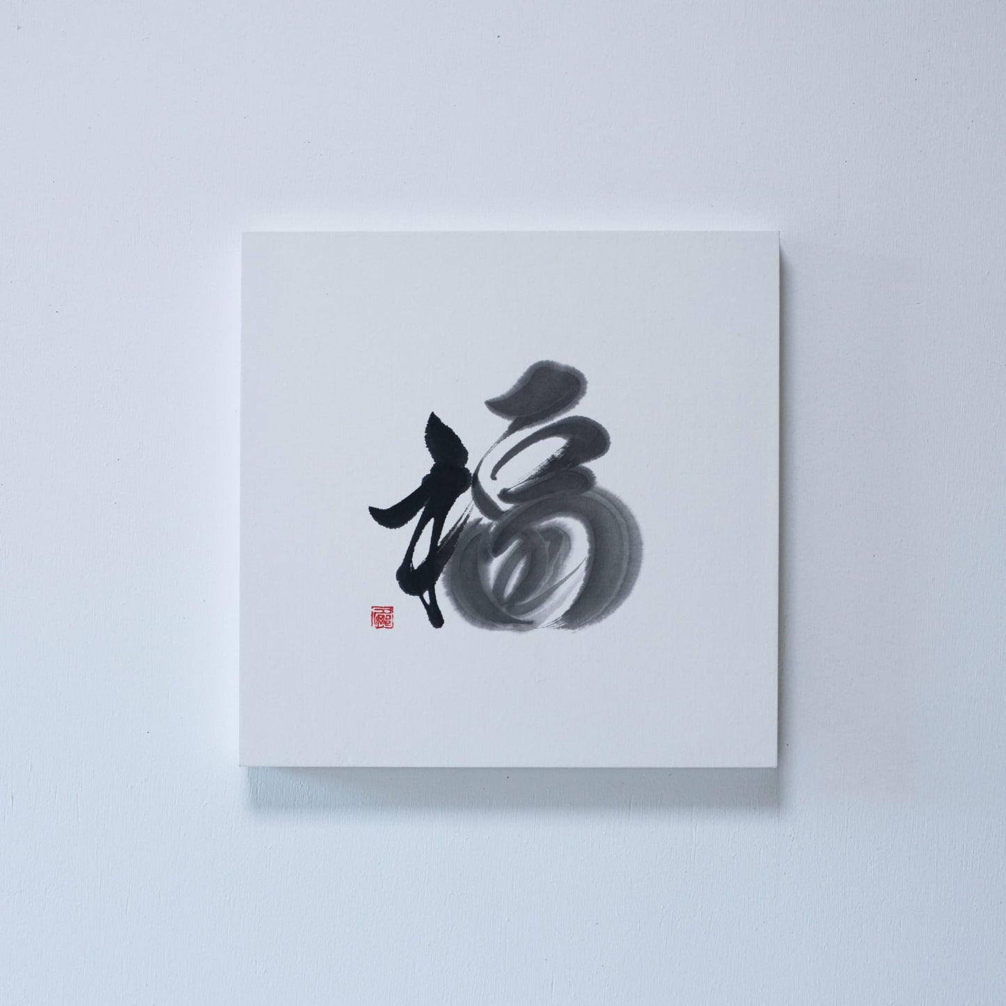 A square panel featuring Japanese calligraphy of the character '福' (fortune) on white rice paper, mounted on a white wall
