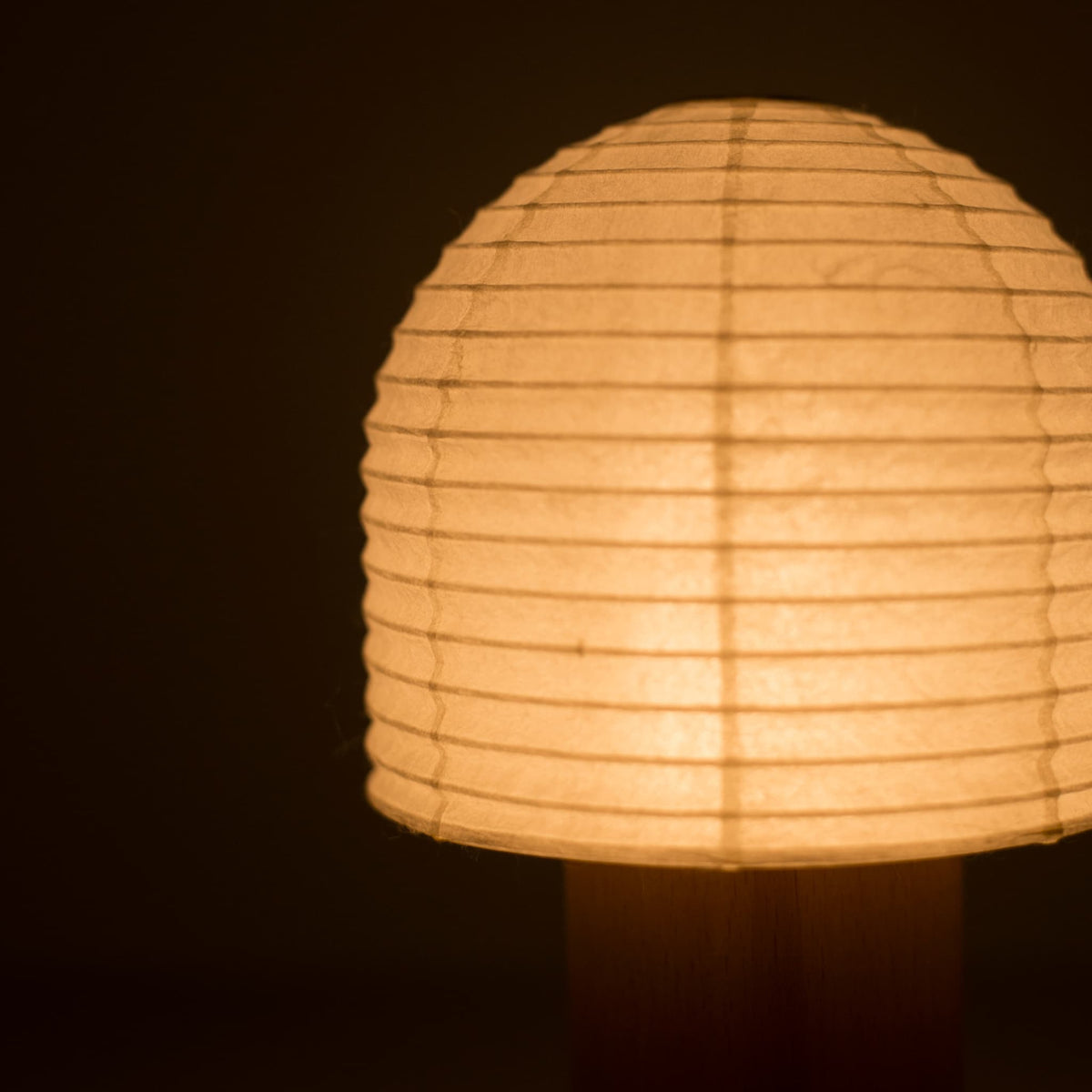 Close-up view of a bell-shaped Yame lantern emitting warm light in a dark room