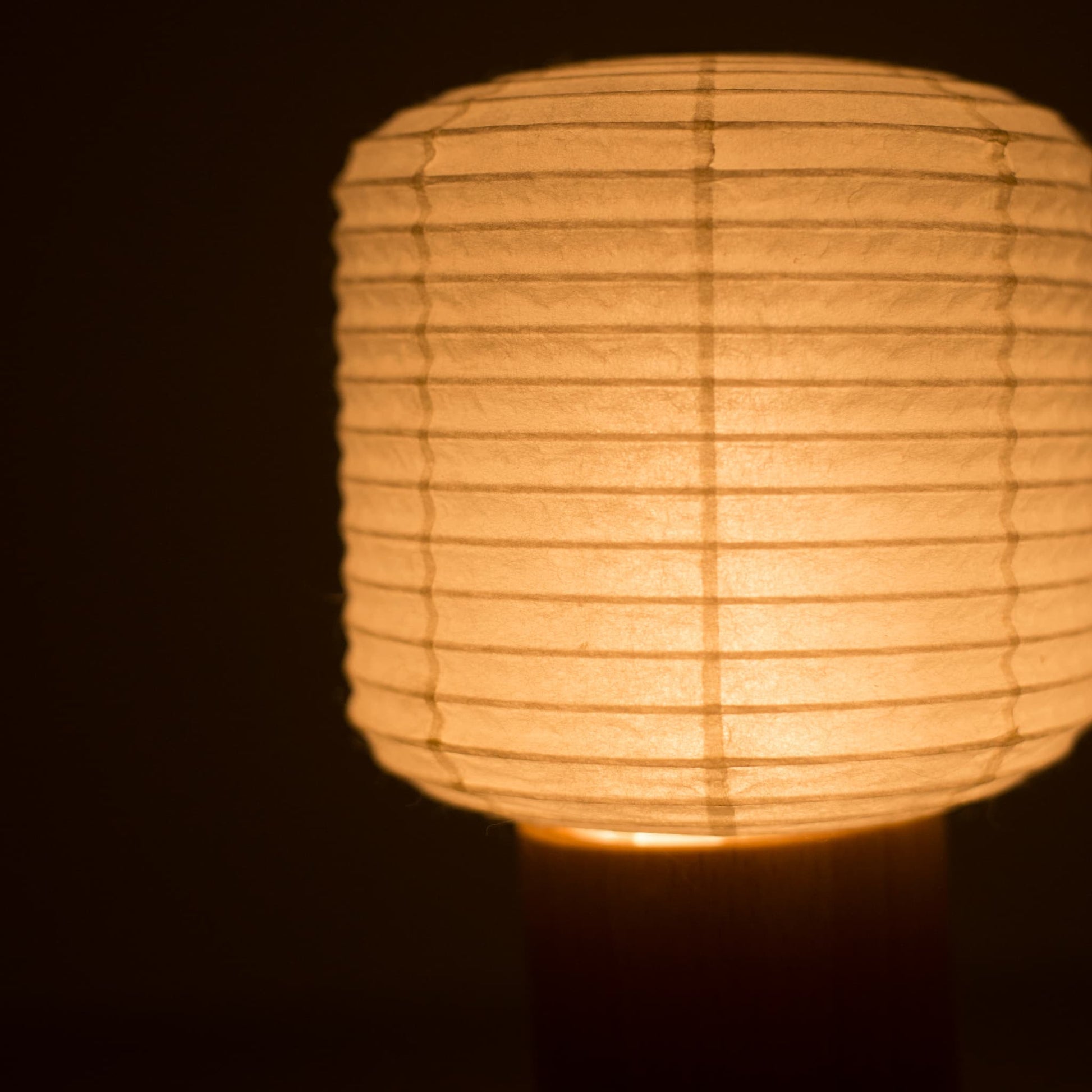 Close-up of the top paper lantern section of a Yame portable light, glowing warm in a dark room