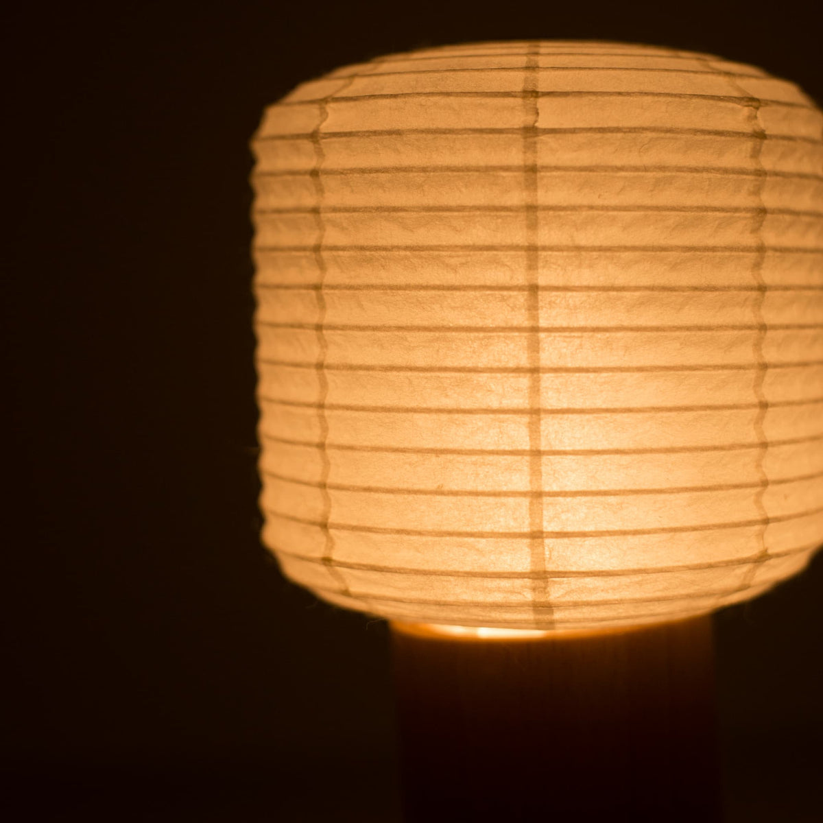 Close-up van het bovenste papieren lampgedeelte van een Yame draagbare lamp, warm gloeiend in een donkere kamer