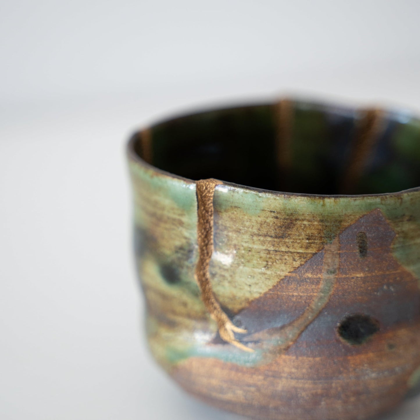 Deep green tea bowl repaired with Kintsugi, a traditional Japanese technique, showcasing the beauty of imperfection.