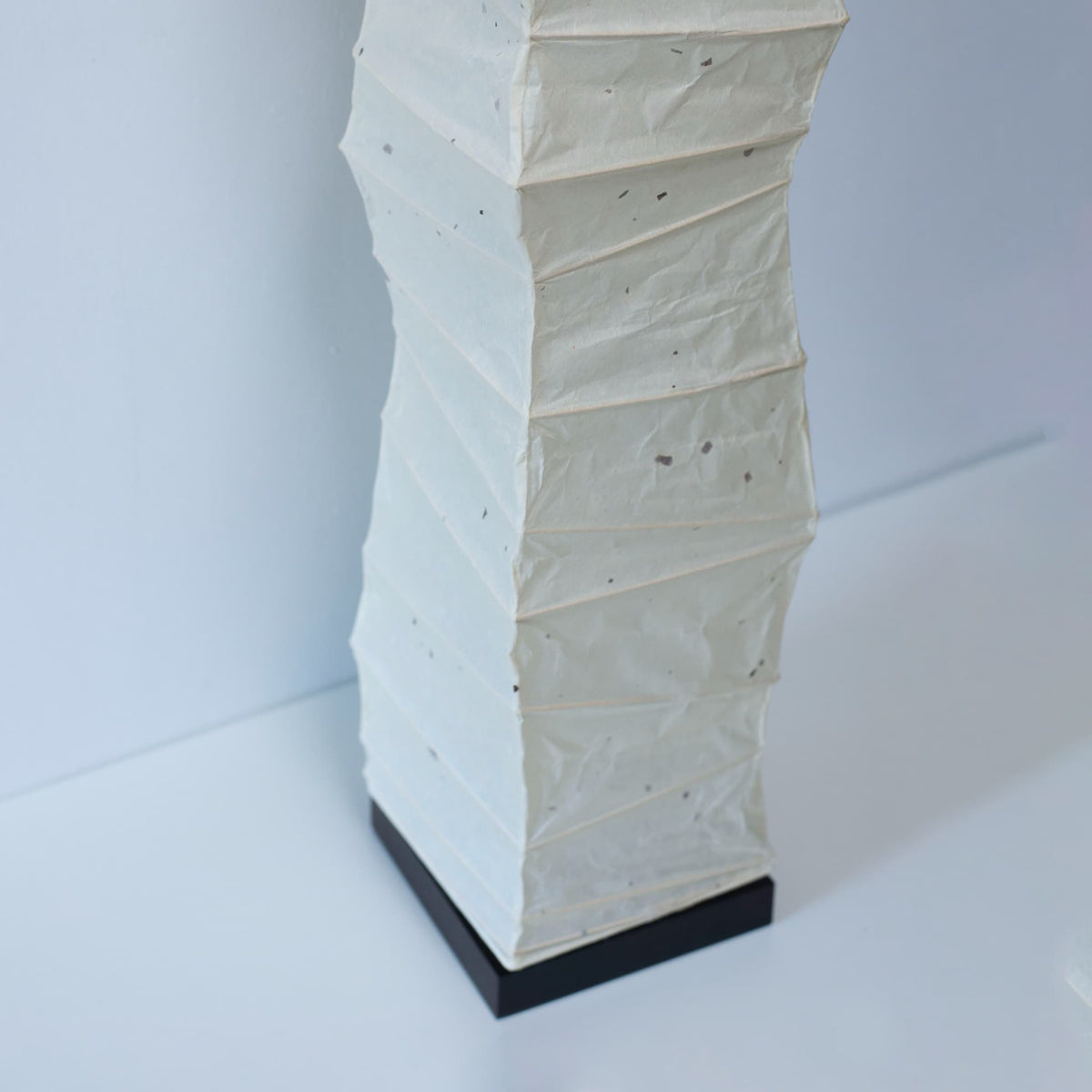 Close-up of the lower section of a curved Japanese washi paper lamp, shot from above on a white background