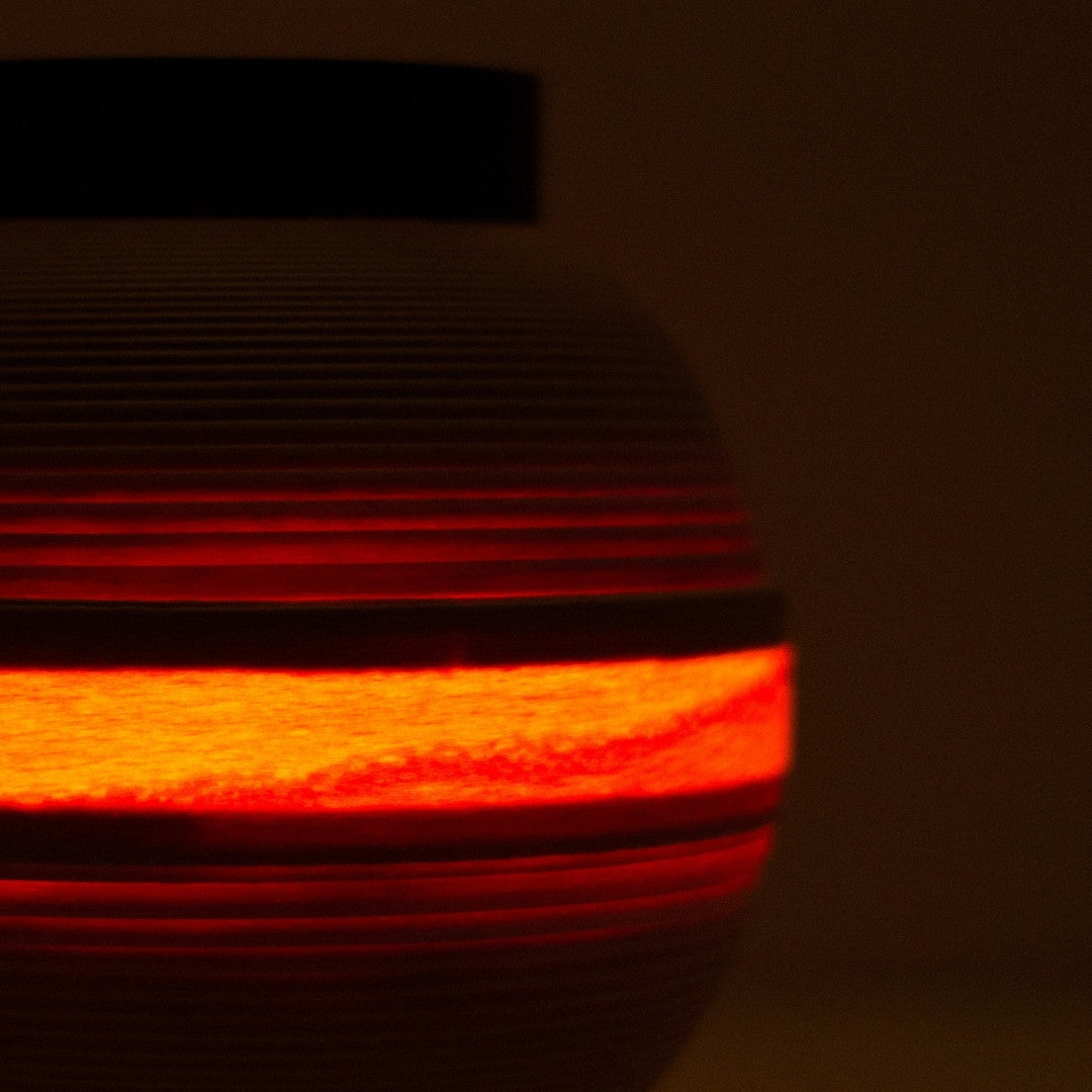 Close-up of Japanese living room lamp with warm light band glowing through beech wood slats.