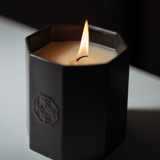 A lit black scented candle made of Arita ware, offering a relaxing wooden fragrance.