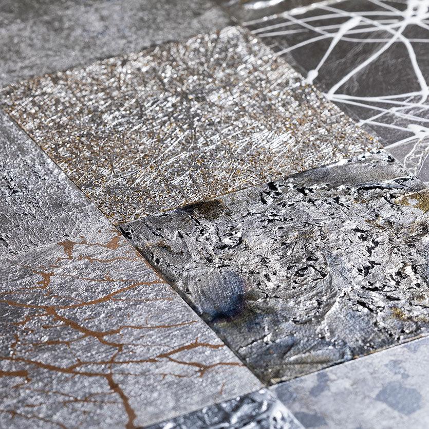 A silver leaf wall art composed of nine panels, each depicting a natural element like wind or rock.