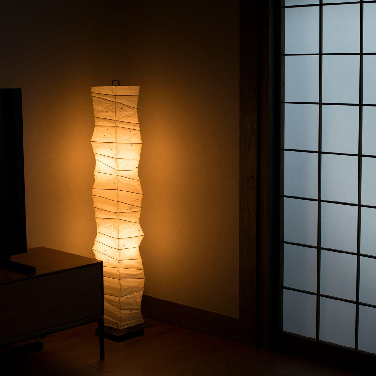 Japanese paper floor lamp with tall, random curves placed in the corner of a traditional Japanese room, emitting a warm light.