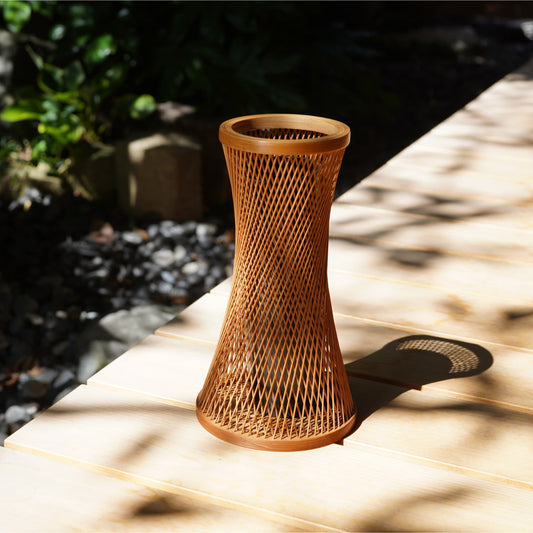 A cylindrical Japanese ikebana vase crafted from bamboo with intricate, interwoven strips, placed on an engawa (veranda).