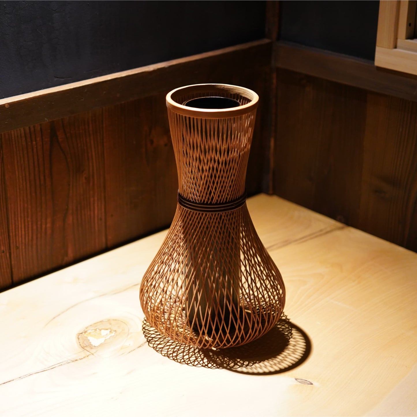 A cylindrical Japanese ikebana vase with a rounded, bulbous base, made from bamboo with beautifully intricate, interwoven strips.