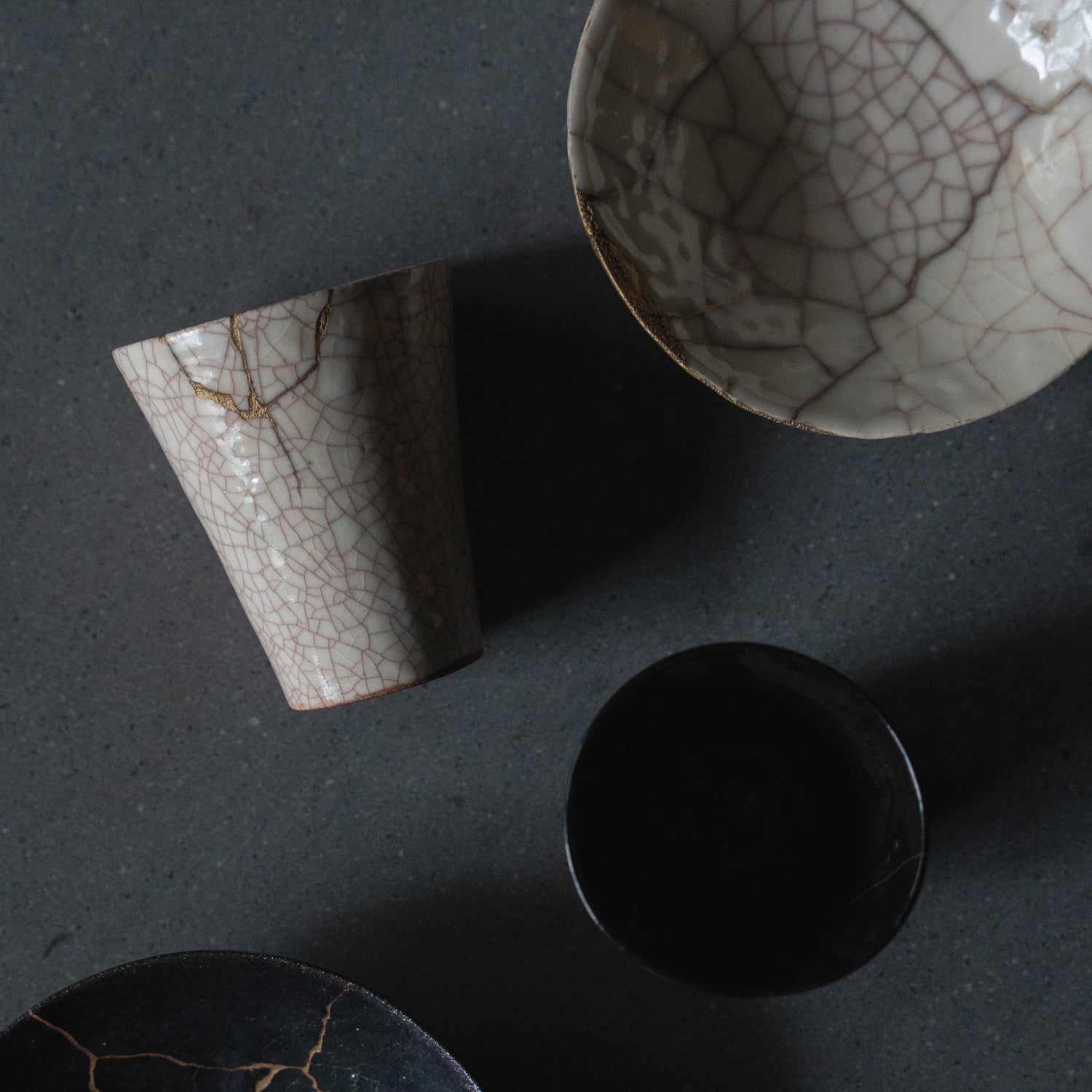 White and black kintsugi cups and bowl, showcasing the traditional Japanese art of repairing broken pottery with gold lacquer.