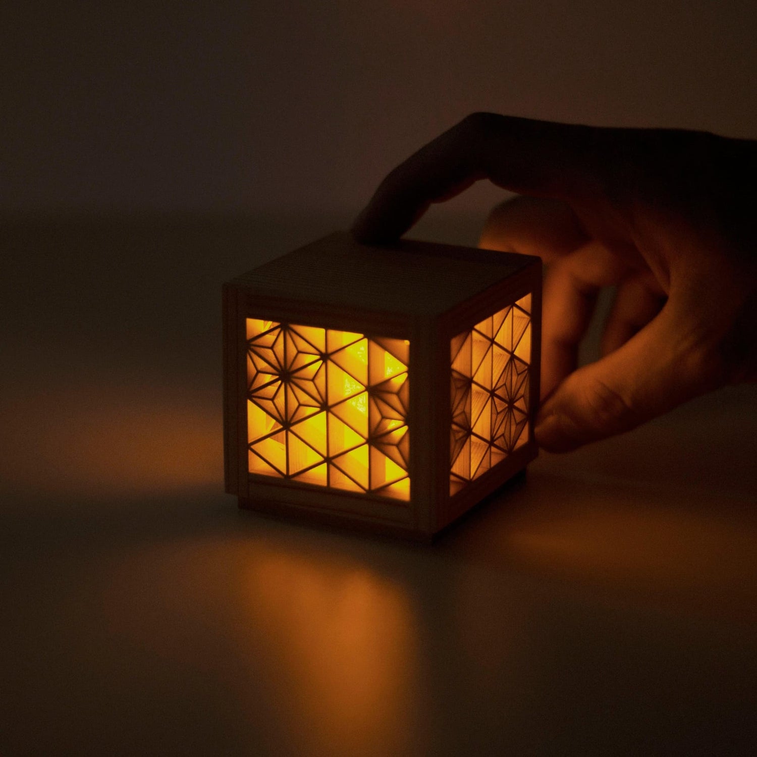 A hand holding a small kumiko lantern. The intricate wooden latticework and warm LED light create a beautiful and inviting scene.
