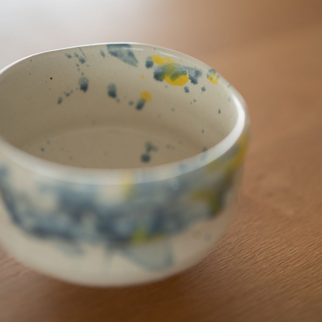Gros plan du bord intérieur du bol à matcha fait main "Splash", mettant en valeur les motifs dynamiques bleus et jaunes créés par une technique spéciale de projection par les artisans de Shinzan Kiln.