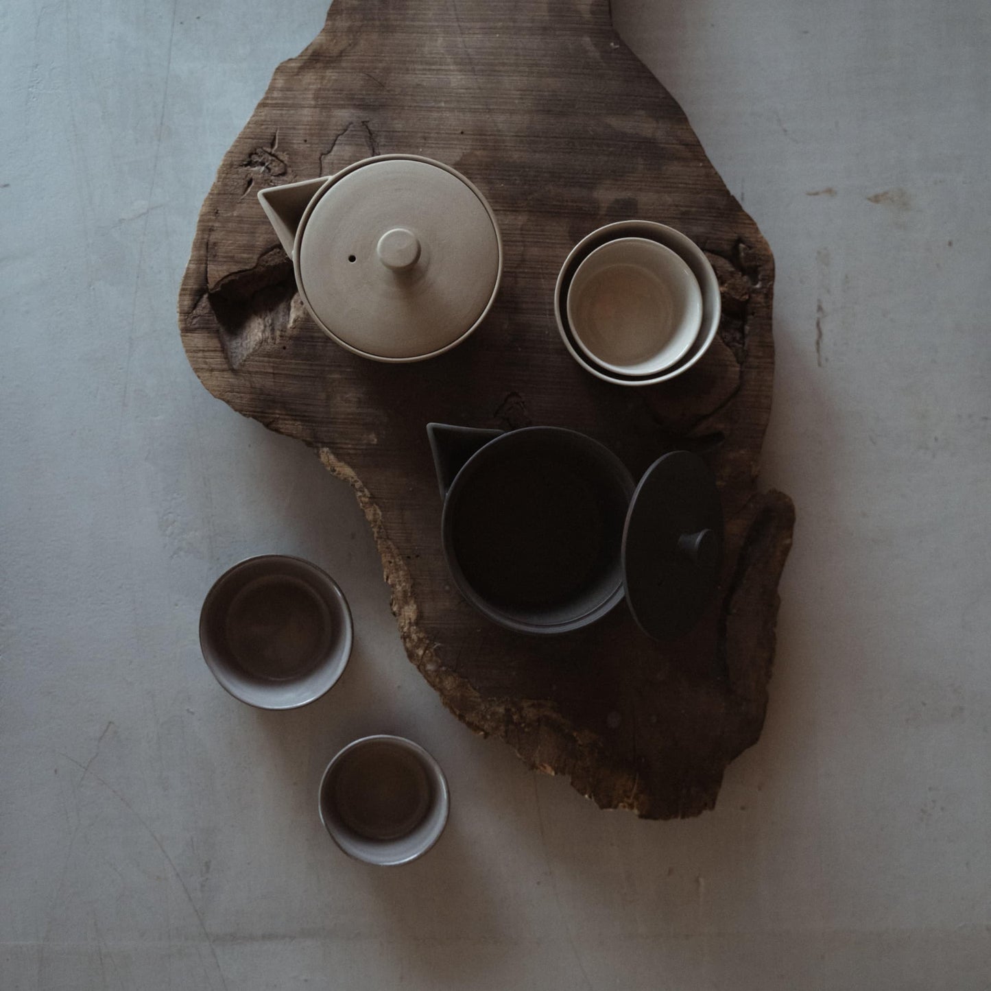 Japandi-style table setting with a wooden table featuring a white and a black Banko-yaki teapot, both crafted using traditional Japanese techniques.