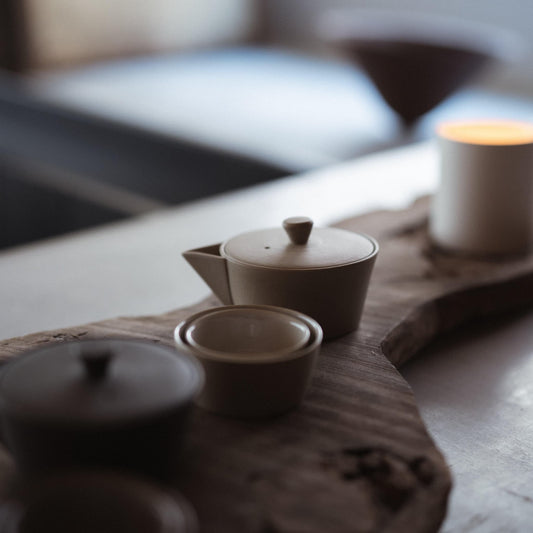 Japandi-style table setting with a wooden table featuring a white and a black Banko-yaki teapot, both crafted using traditional Japanese techniques.