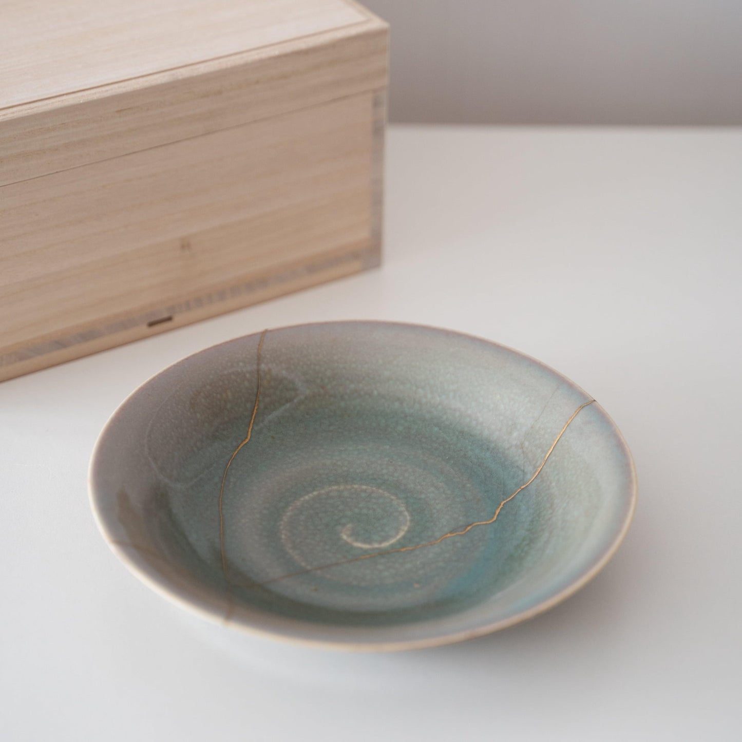 Gift set of a pale green bowl repaired with Kintsugi, a traditional Japanese technique, and a paulownia wood box.