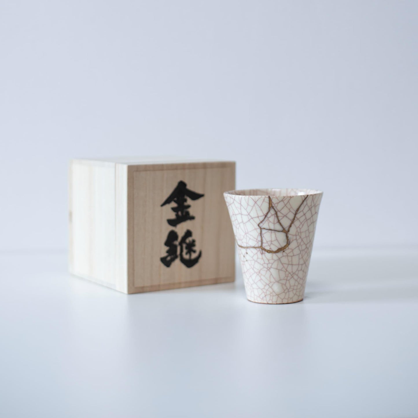 White cup repaired with Kintsugi, a traditional Japanese technique, presented in a paulownia wood box with the inscription "Kintsugi".
