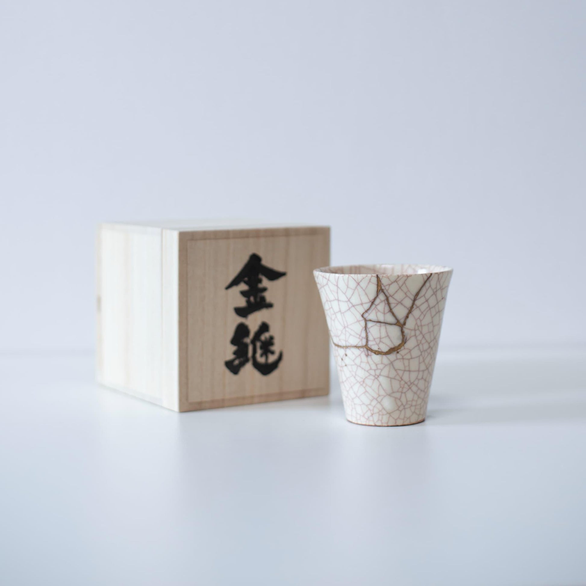 White cup repaired with Kintsugi, a traditional Japanese technique, presented in a paulownia wood box with the inscription "Kintsugi".