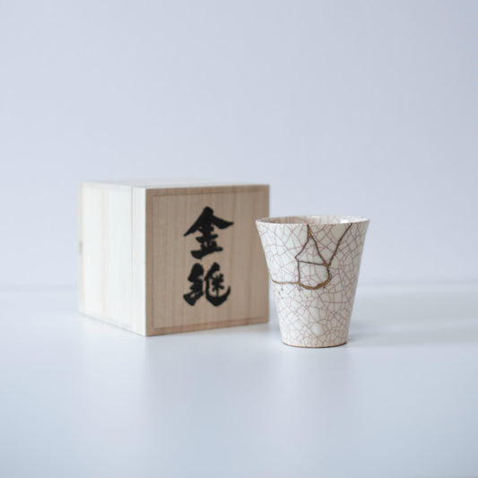 White cup repaired with Kintsugi, a traditional Japanese technique, presented in a paulownia wood box with the inscription "Kintsugi".