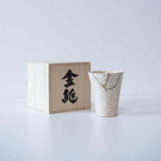 White cup repaired with Kintsugi, a traditional Japanese technique, presented in a paulownia wood box with the inscription "Kintsugi".