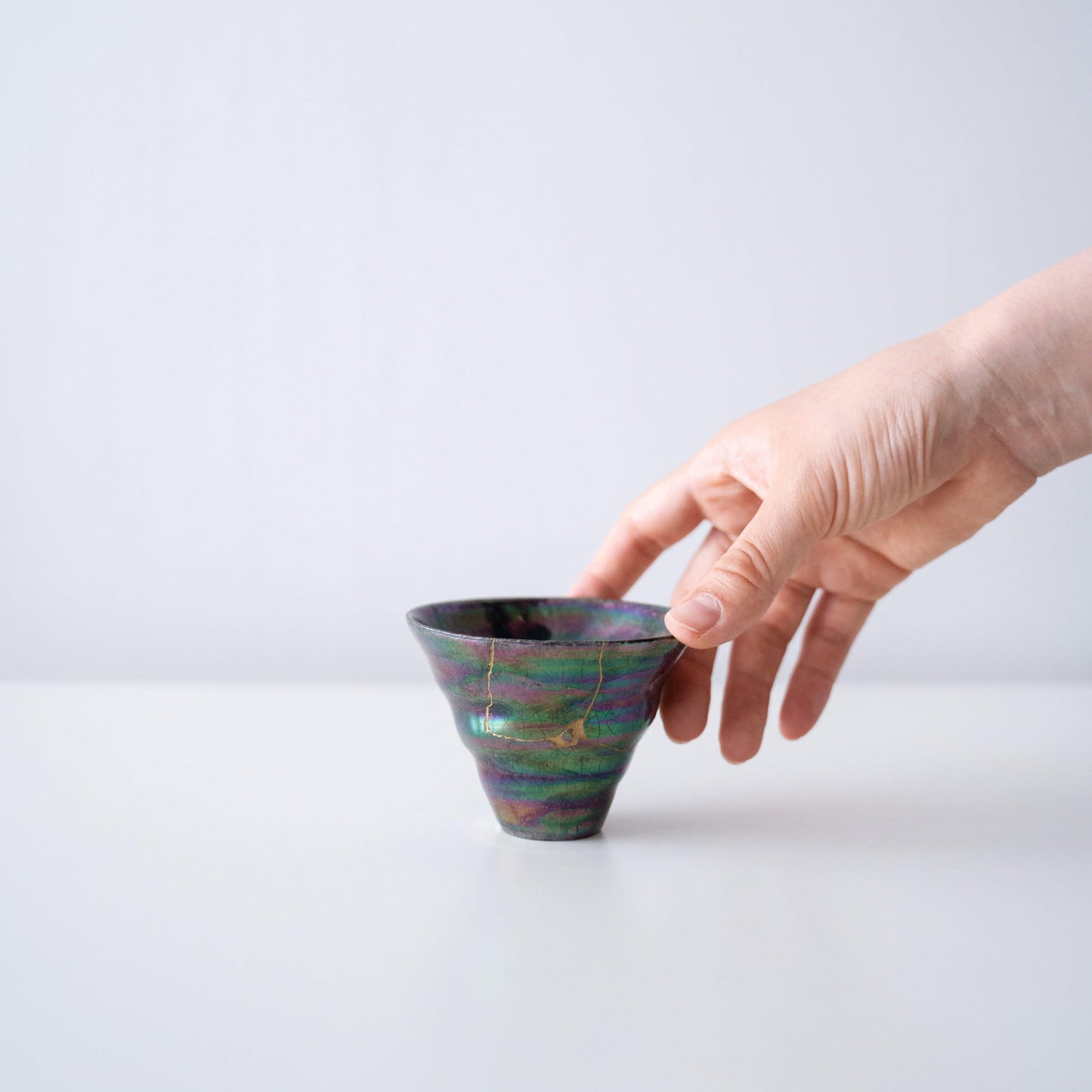Hand holding an iridescent coral-shaped cup repaired with Kintsugi, a traditional Japanese technique.
