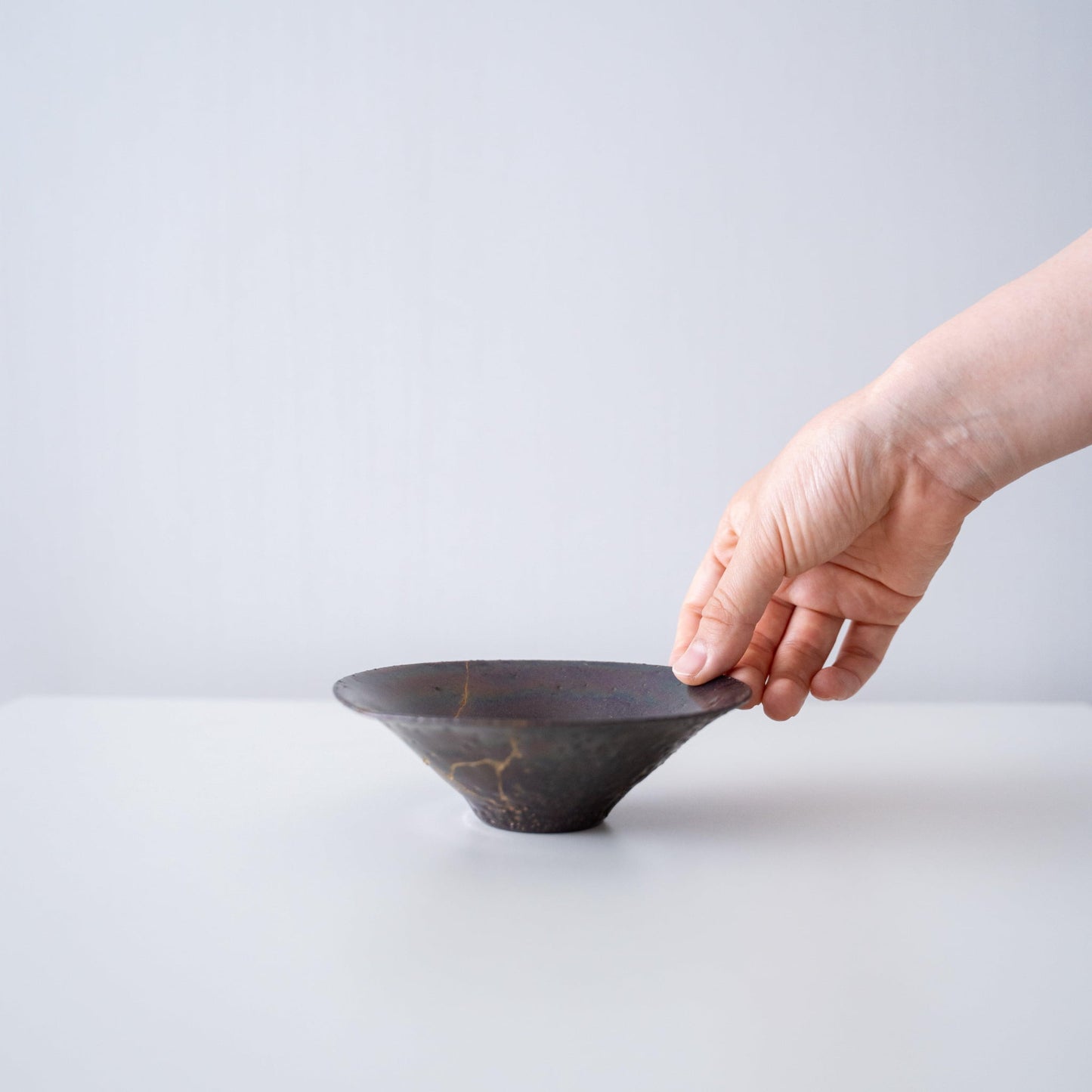 Hand holding a leaf-shaped bowl repaired with Kintsugi, a traditional Japanese technique.