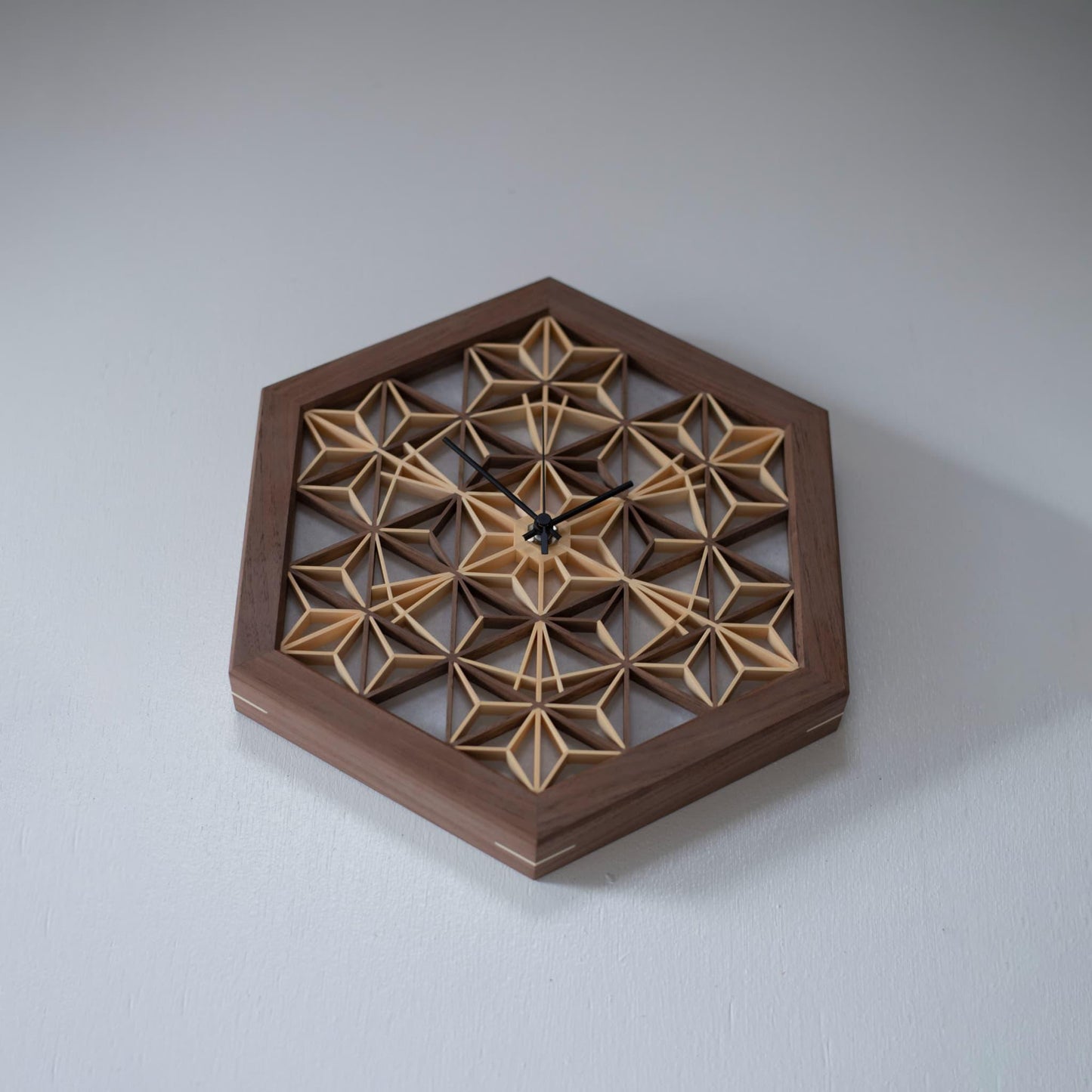 A walnut kumiko clock hanging on a wall, viewed from below. The intricate wooden latticework creates a warm and inviting atmosphere.