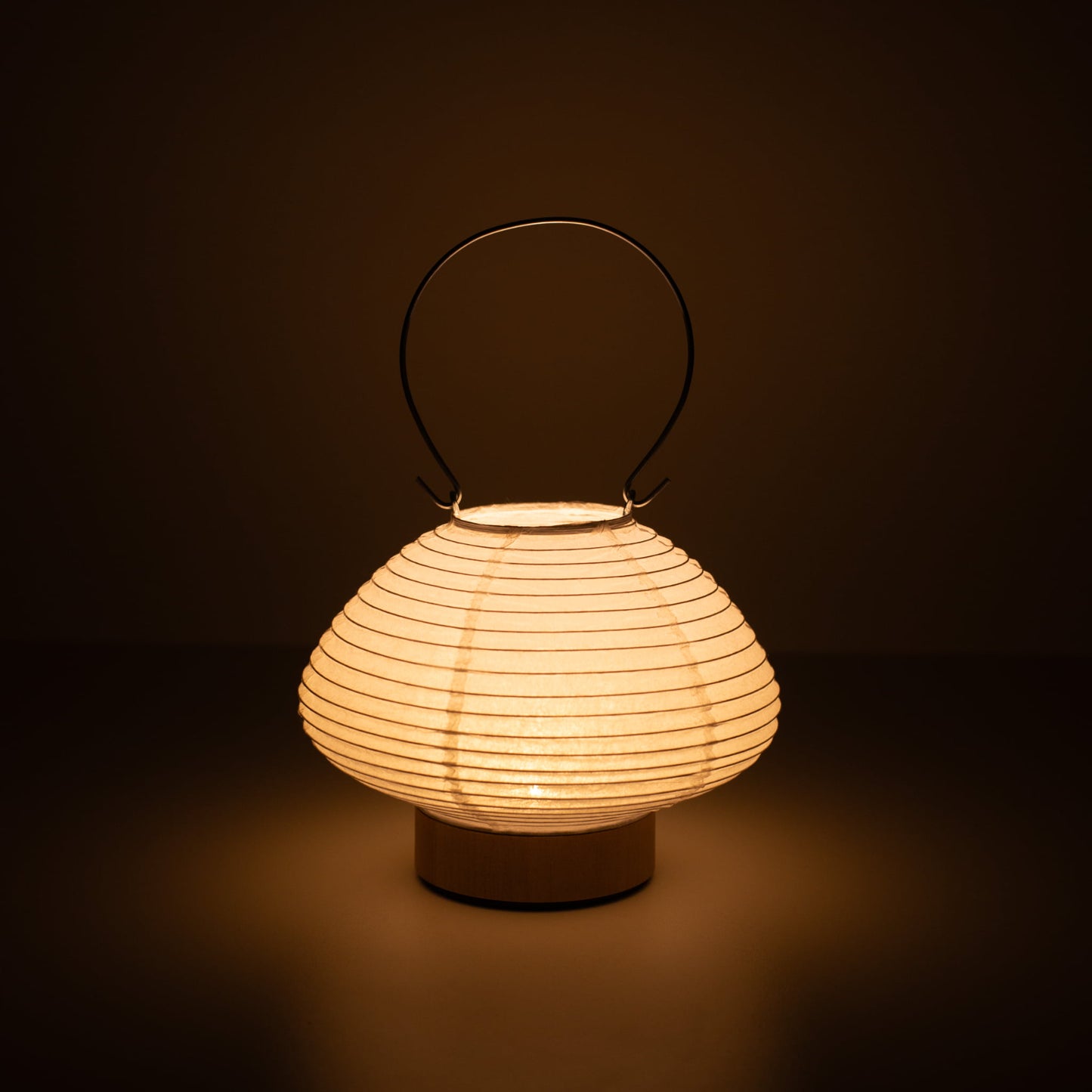 Hand holding a portable paper table lamp resembling a traditional Japanese lantern, crafted with Gifu lantern techniques and Mino washi paper.