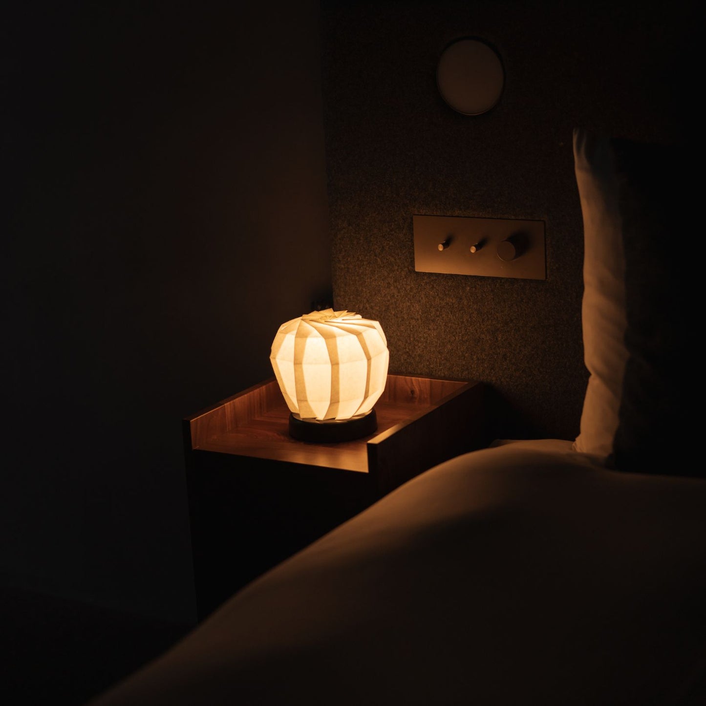 Japanese Origami Paper Table Lamp "Flower of Light" - maru M emitting warm light on a bedside table in a Japandi bedroom.