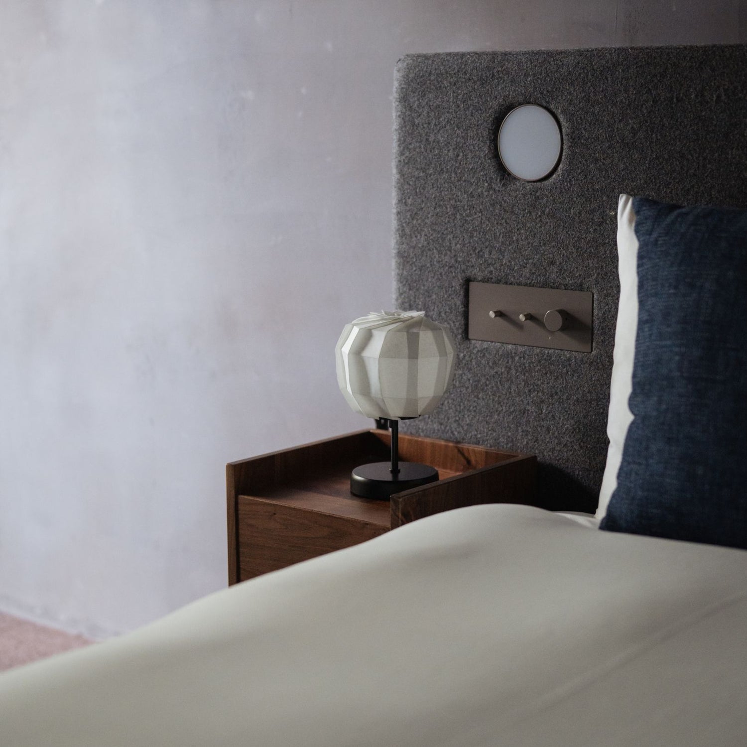 A Japanese Origami Paper Lamp "Flower of Light" maru with stand on a bedside table.