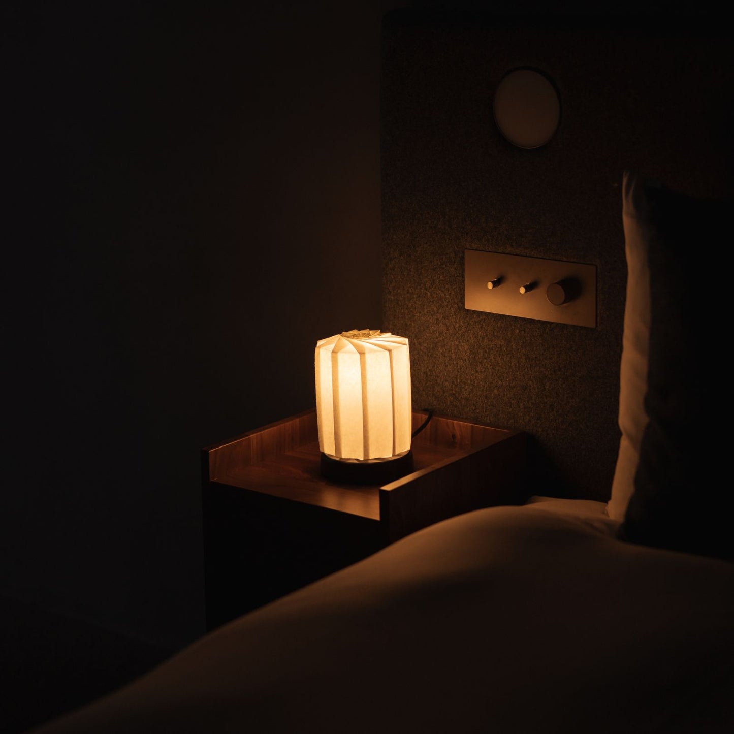 Japanese Origami Paper Table Lamp "Flower of Light" - tutu M emitting warm light on a bedside table in a Japandi bedroom.