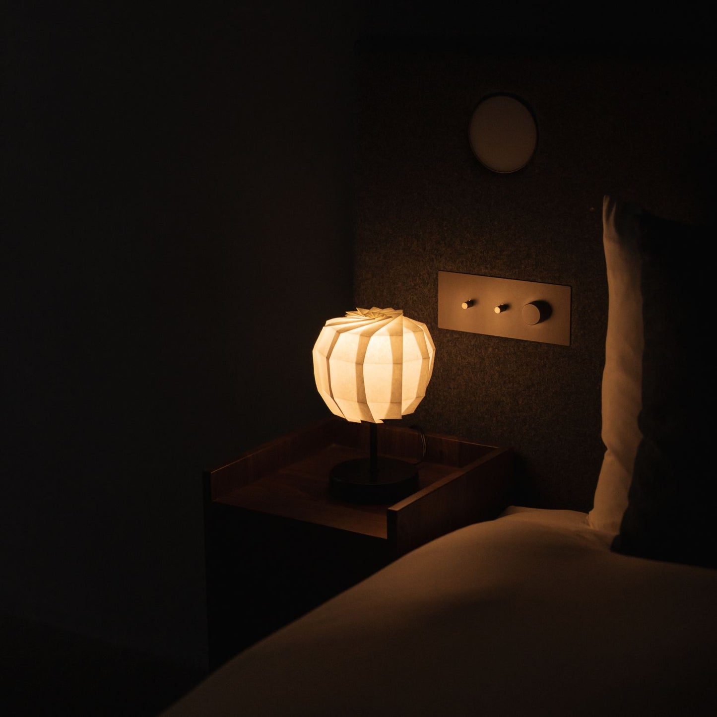 Japanese Paper Table Lamp "Flower of Light maru with Stand" lit on a wooden bedside table