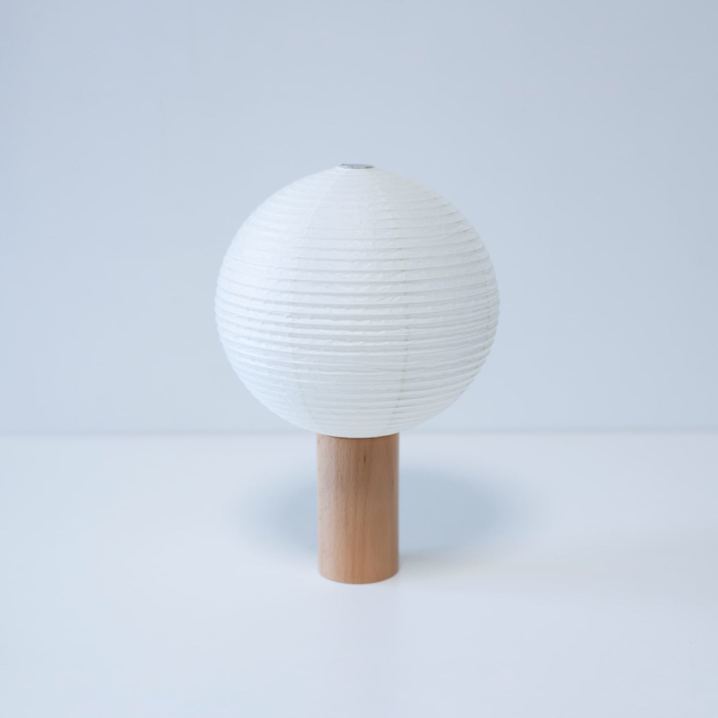 Paper table lamp "TORCHIN CIRCLE" with a unique spherical white washi paper shade and a wooden handle, handcrafted using traditional Yame lantern techniques in Fukuoka, Japan.