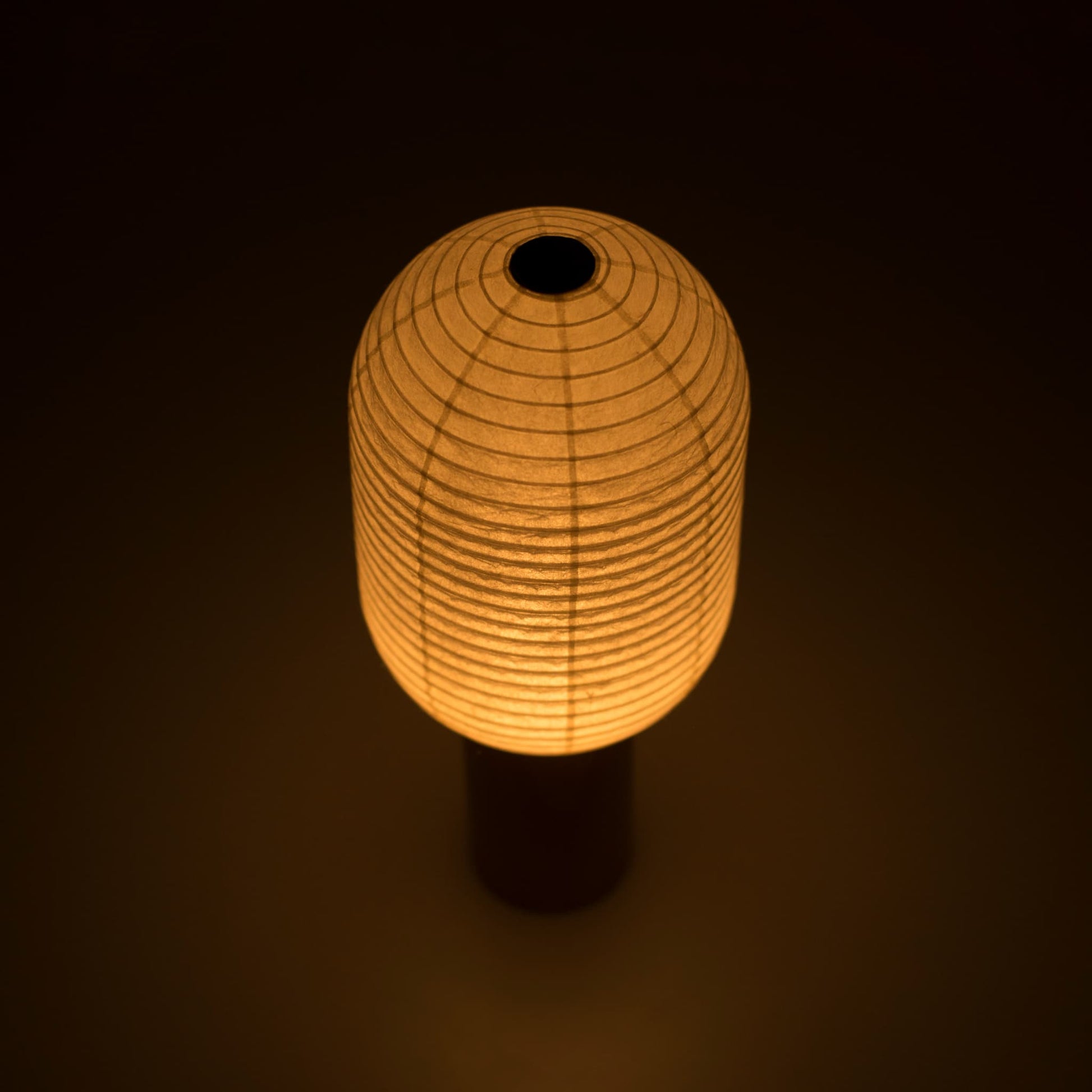 Portable paper lamp "TORCHIN VERTICAL" emitting a warm glow, handcrafted in Yame, Fukuoka, Japan, known for its traditional Yame lanterns.
