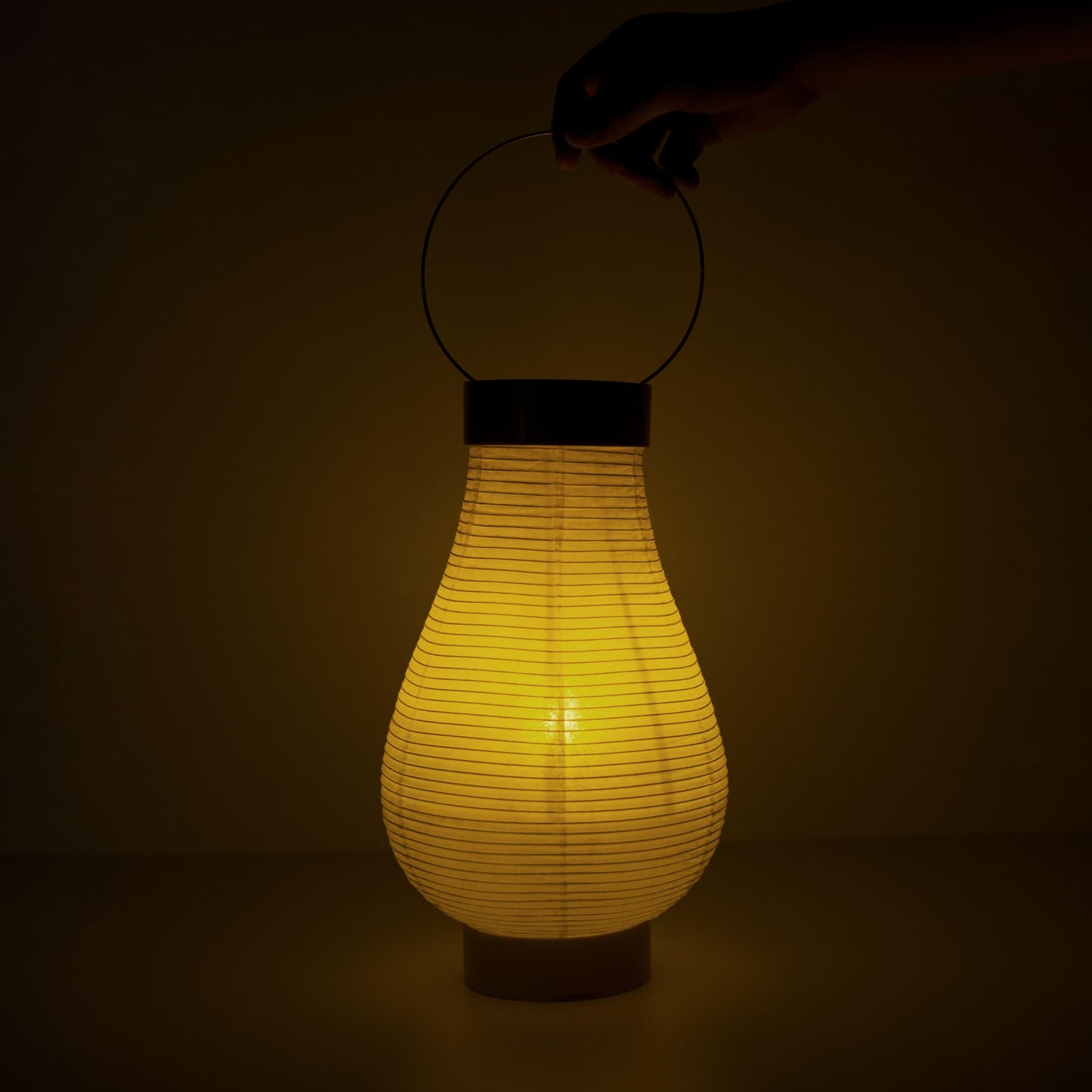 A traditional Japanese paper lantern with warm lighting and a hand visible in a dark room
