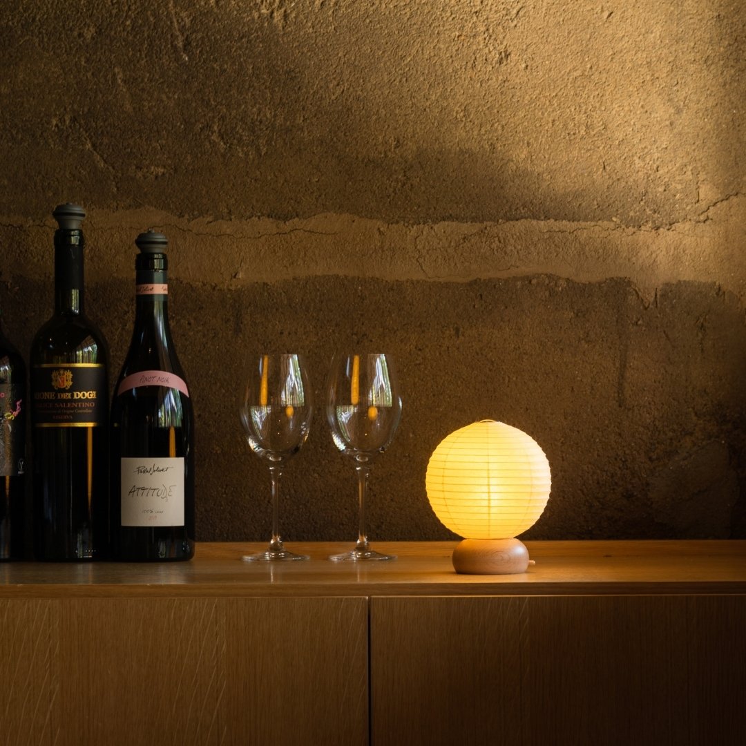 Japanese Paper Table Lamp "Mini Circle" with wine bottles and wine glasses on a wood shelf on corner in a room