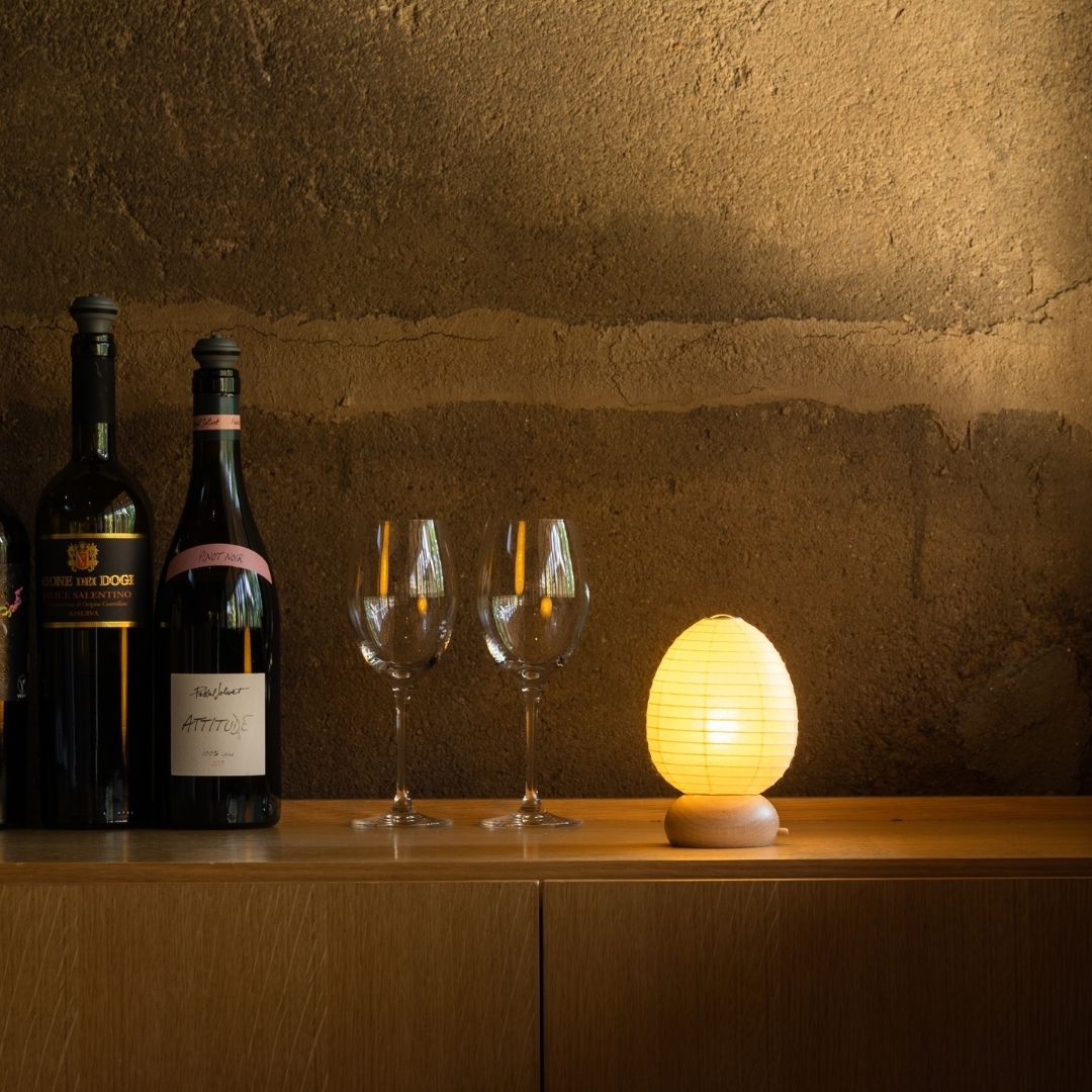 Japanese Paper Table Lamp "Mini Egg" with wine bottles and wine glasses on a wood shelf on corner in a room