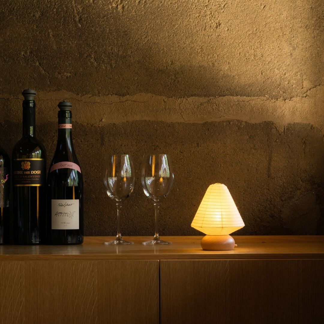 Japanese Paper Table Lamp "Mini Triangle" with wine bottles and wine glasses on a wood shelf on corner in a room