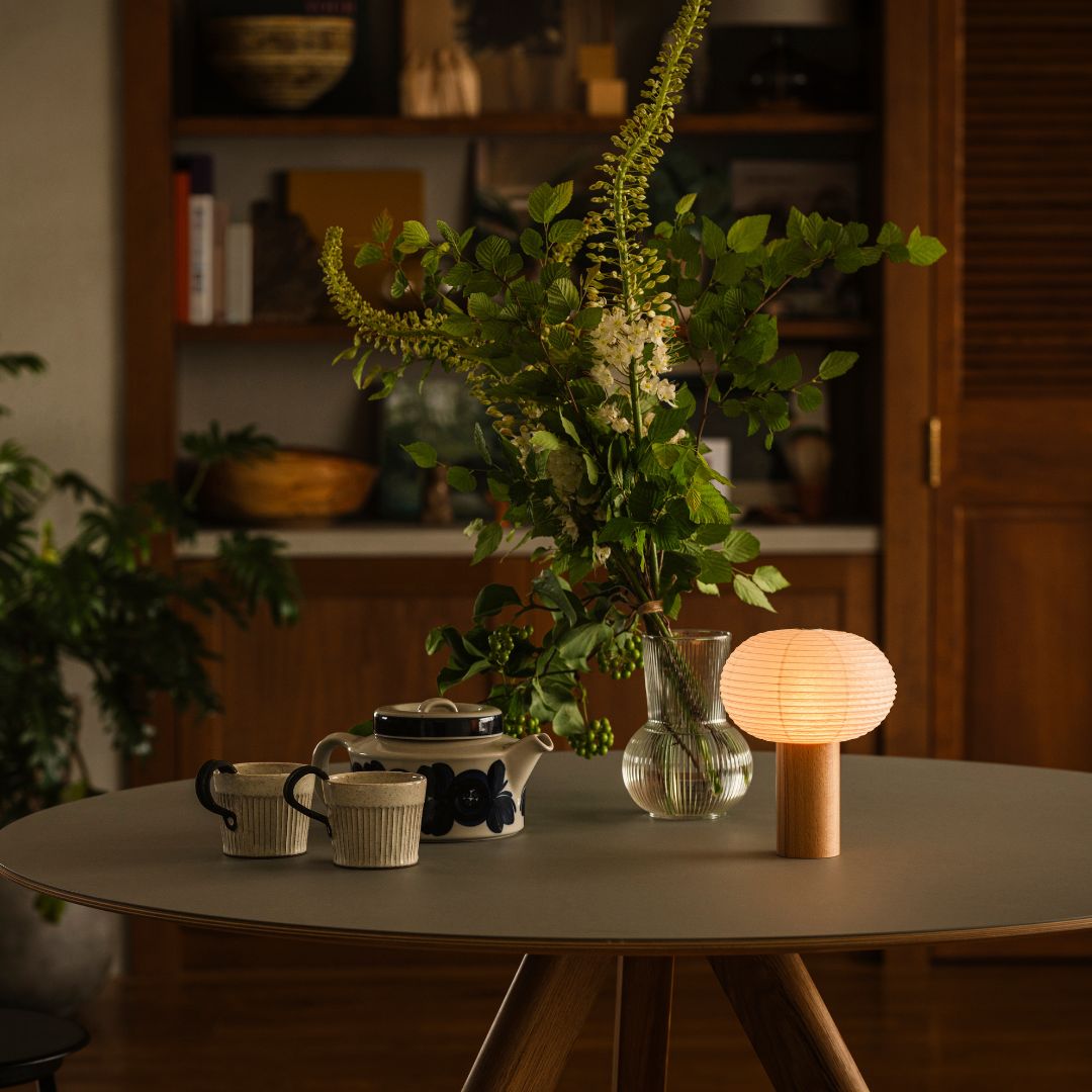The portable paper table lamp TORCHIN OVAL is lit, emitting a warm lamp on a grey table in living room.