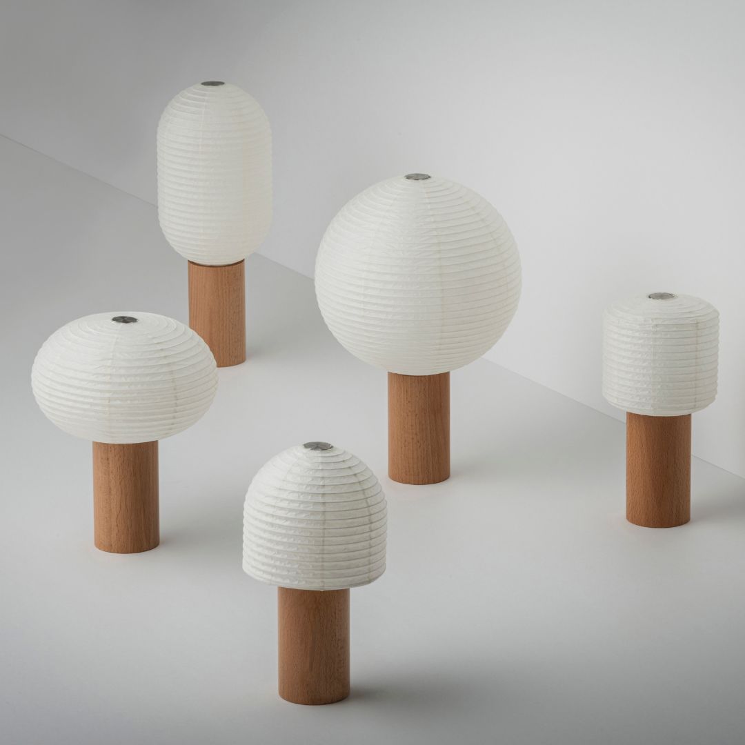 Five paper table lamps, "TORCHIN", with beautiful white washi paper and brown wooden handles, randomly arranged in a bright white room. The lampshades are made of Japanese washi paper from Yame-chochin lanterns, and each lamp has a wooden cylindrical handle.